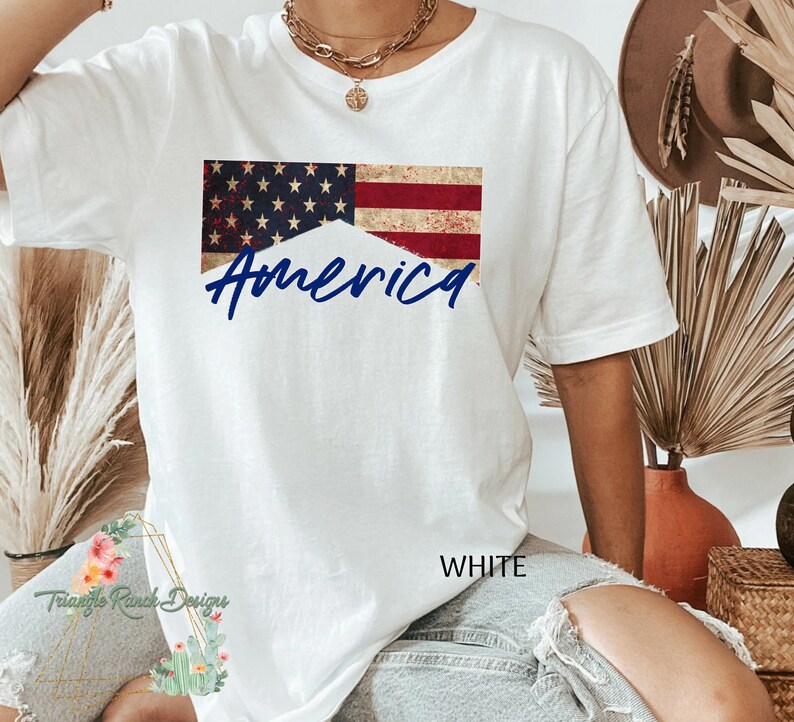 May include: White t-shirt with a distressed American flag design and the word "America" in blue lettering.