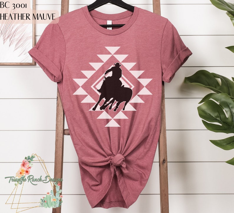 Pu&ograve; includere: Una t-shirt color malva sfumato con la silhouette di un cowboy che cavalca un toro infuriato all'interno di uno schema geometrico.