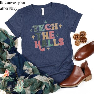 May include: A heather navy blue t-shirt with the text "Tech the Halls" in colorful retro lettering. The text is surrounded by small white stars.