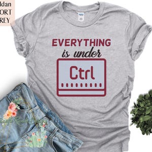 Puede incluir: Una camiseta gris con el texto "Everything is under Ctrl" impreso en rojo en la parte delantera. El texto está estilizado para parecer una tecla de teclado de computadora.