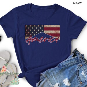 May include: A navy blue t-shirt with a distressed American flag and the word "America" in red script.