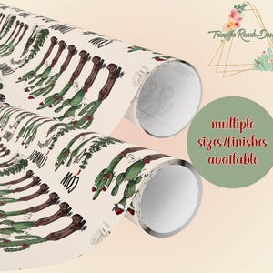 May include: A roll of wrapping paper with a cactus and cowboy boot design. The paper is cream colored with green cacti and brown cowboy boots. The text "MOO" and "COWBOY" is printed on the paper.