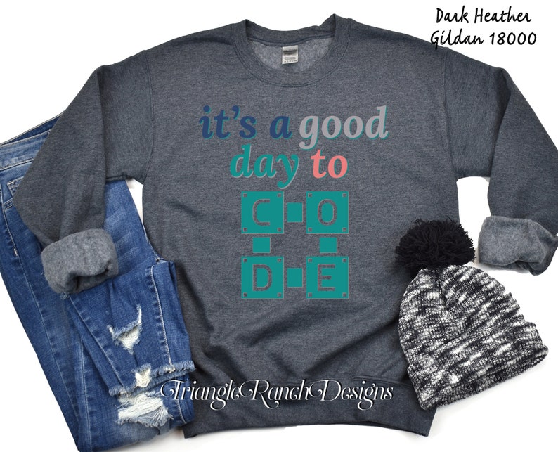 K&ouml;nnte beinhalten: Dunkelgraues Sweatshirt mit dem Text "it's a good day to CODE" in T&uuml;rkis, Rosa und Grau. Das Sweatshirt wird mit einer blauen Jeans und einer schwarz-wei&szlig; gestrickten M&uuml;tze mit einem schwarzen Bommel pr&auml;sentiert. Der Markenname "Triangle Ranch Designs" steht unten.