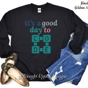 K&ouml;nnte beinhalten: Schwarzes Sweatshirt mit dem Text "it's a good day to CODE" in Blau- und Gr&uuml;nt&ouml;nen. Das Design zeigt ein gitterartiges Muster mit den Buchstaben C, O, D und E. Das Sweatshirt wird mit blauen Jeans gezeigt.