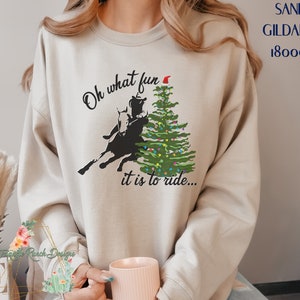 May include: A beige sweatshirt with the text "Oh what fun it is to ride..." and a silhouette of a person riding a horse in front of a Christmas tree with a Santa hat on top.