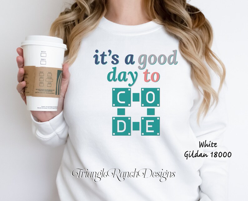 K&ouml;nnte beinhalten: Wei&szlig;es Gildan 18000 Sweatshirt mit dem Text "it's a good day to CODE" in T&uuml;rkis, Rosa und Blau. Das Design zeigt eine quadratische Grafik mit den Buchstaben C, O, D und E. Eine Kaffeetasse wird im Bild gehalten.