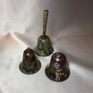 Puede incluir: Tres campanas decorativas con intrincados patrones florales en tonos de azul, rojo, verde y dorado. Las campanas están hechas de latón y tienen un acabado de esmalte cloisonné.