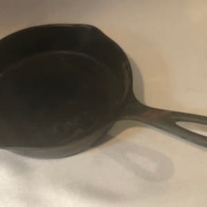 May include: A cast iron skillet with a black handle. The skillet is worn and has a dark patina.