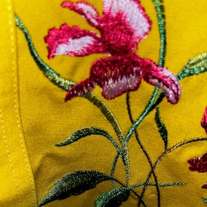 May include: Close-up of a yellow fabric with embroidered pink and white flowers and green leaves.