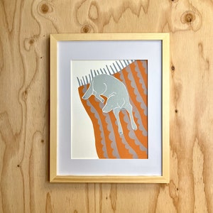 May include: A framed print of a grey dog sleeping on an orange and grey patterned blanket.