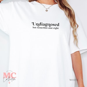 May include: White oversized t-shirt with the text "Undiagnosed but somethin aint right" printed in black. The shirt has a crew neck and short sleeves.