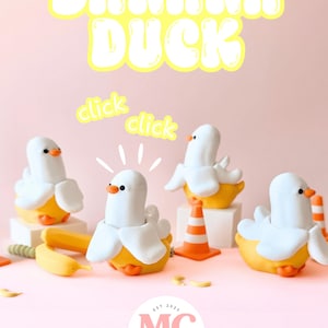May include: Four white and yellow banana duck figurines with orange beaks and feet, arranged with miniature orange traffic cones and a banana peel. The text BANANA DUCK appears at the top, with the word click repeated twice and a logo at the bottom.