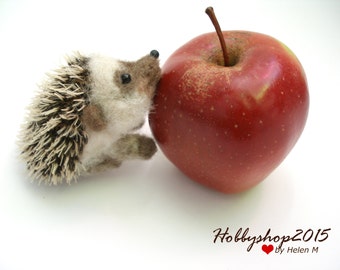 May include: A small, brown and white hedgehog figurine next to a red apple. The hedgehog has a spiky back and a cute face.