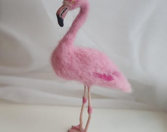 Puede incluir: Escultura artesanal de un flamenco rosa con un cuello largo y curvado y patas delgadas. El ave tiene un pico negro, ojos amarillos y una textura esponjosa. El flamenco está sobre una superficie blanca.