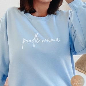 Può includere: Felpa blu chiaro con il testo "poodle mama" in corsivo bianco.