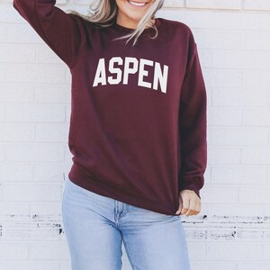 May include: A maroon sweatshirt with the word "ASPEN" printed in white on the front.