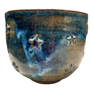 May include: A ceramic bowl featuring a deep blue and brown mottled glaze with embossed star shapes scattered across the exterior surface. The bowl has a rounded silhouette and a smooth, glossy finish that highlights the color variations.