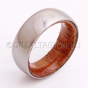 May include: A silver ring with a wooden inlay. The wood is a reddish brown color and has a natural grain pattern. The ring is polished and has a shiny finish.