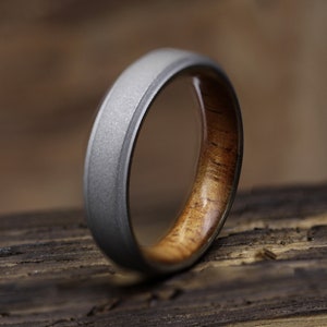 Puede incluir: Un anillo de plata y madera con acabado cepillado. El anillo está hecho de titanio y madera.