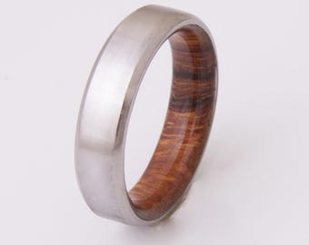 May include: A silver and brown wood ring with a beveled edge. The ring is made of titanium and wood.