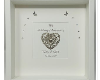 May include: A framed wedding anniversary keepsake. The white frame surrounds a white background with a silver heart-shaped ornament. The text reads "TIN Wedding Anniversary" and the names "Helen & Nick" with the date "9th May 2021". Decorative butterflies and crystals are also included.