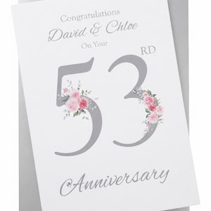 May include: A white anniversary greeting card with a silver envelope. The card features the text Congratulations David & Chloe On Your 53rd Anniversary in grey font. The large number 53 is decorated with pink floral illustrations and crystals.