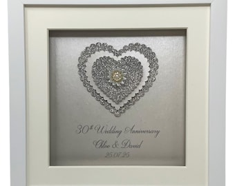 May include: A white frame with a silver glitter heart inside. The heart has a pearl-like center and the text "30th Wedding Anniversary Chloe & David 25.07.25" is written below the heart.