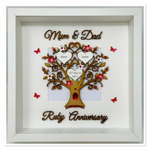 Può includere: Un albero genealogico in legno incorniciato in bianco con le parole "Mum & Dad" e "Ruby Anniversary". L'albero presenta foglie a forma di cuore con nomi e una data, decorato con fiori e farfalle rosse.