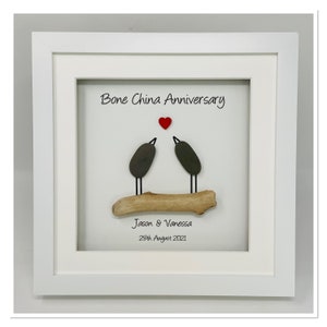 May include: A framed artwork featuring two pebble birds perched on a driftwood branch, with a red heart above them. The text "Bone China Anniversary" is written above the birds, and "Jason & Vanessa 28th August 2021" is written below.
