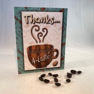 以下が含まれることがあります： ハート型の蒸気を立てた茶色のコーヒーカップが描かれた、ありがとうカード。カードは薄い青色の背景にコーヒー豆の模様が描かれており、「ありがとう&hellip; A-Latte!」という文字が書かれています。