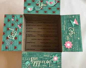May include: A teal and red patterned cardboard box with the words "Loved", "You", "Incredibly", and "Are" on the sides. The box is open and the inside is decorated with a similar pattern.