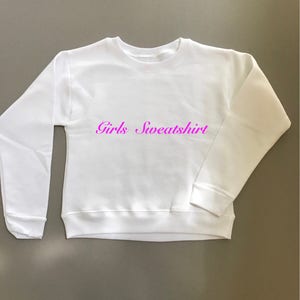 May include: White sweatshirt with the text "Girls Sweatshirt" in pink lettering.