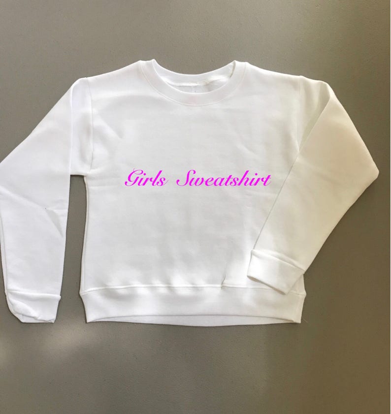 May include: White sweatshirt with the text "Girls Sweatshirt" in pink lettering.