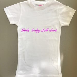 May include: White baby doll shirt with the text "Girls baby doll shirt" printed in pink.