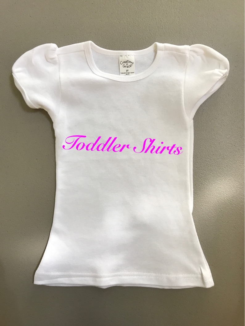 May include: White toddler shirt with a pink "Toddler Shirts" text on the front.