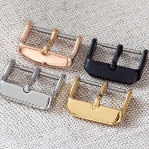 May include: Four watch strap buckles in different finishes: rose gold, silver, black, and gold.