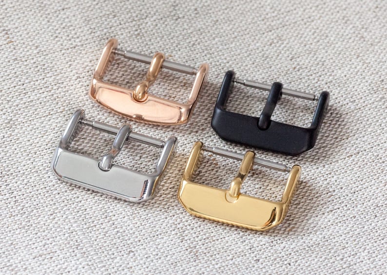 May include: Four watch strap buckles in different finishes: rose gold, silver, black, and gold.