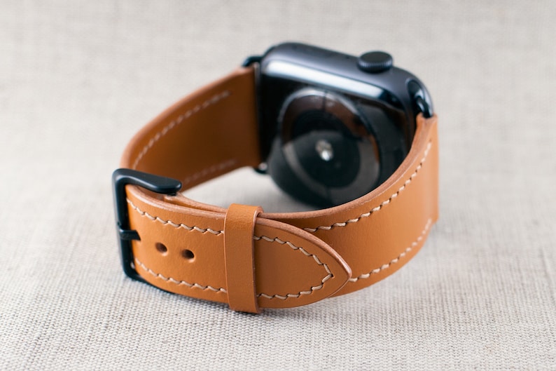 May include: A brown leather watch strap with white stitching. The strap is designed for an Apple Watch and has a black metal buckle.