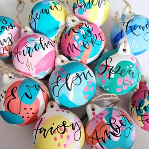 Gepersonaliseerde kerstballen: handgeschilderde kleurrijke kerstversieringen, boodschap en naam in kalligrafie, eerste kerstbal.