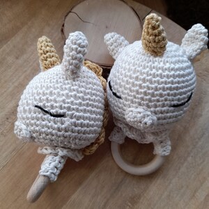 May include: Two crocheted unicorn rattle toys with wooden rings. The unicorns are white with yellow yarn horns and black embroidered eyes.