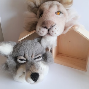 Peut inclure: Un loup gris et un lion blanc aux yeux orange, tous deux en feutre, sont présentés dans un cadre en bois en forme de maison.