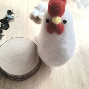 Peut inclure: Un poulet en feutre blanc avec une crête rouge et un bec jaune. Le poulet est assis sur une tranche de bois de rondin.