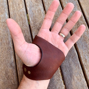 Peut inclure: Un protège-doigts de tir à l'arc en cuir marron avec des rivets en laiton. Le protège-doigts est conçu pour protéger les doigts lors du tir à l'arc. Le cuir est d'un brun foncé riche.