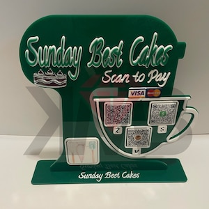 Puede incluir: Un soporte verde con forma de batidora de pie con las palabras "Sunday Best Cakes" y "Scan to Pay" en letras blancas. El soporte tiene una taza blanca con tres códigos QR y las palabras "VISA" y "MasterCard" en letras blancas.