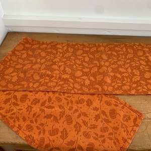 May include: Orange table runner with a pumpkin and leaf pattern.