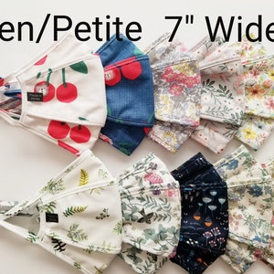 Op de afbeelding: Assortiment van 17,8 cm brede gezichtsmaskers in verschillende bloemen- en patroondesigns. De maskers zijn gemaakt van stof en hebben verstelbare oorlussen. De tekst "Teen/Petite 7" Wide" is zichtbaar bovenaan de afbeelding.