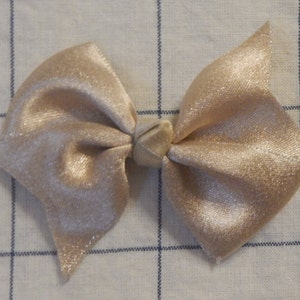 May include: A large, beige satin bow with a center knot. The bow has a subtle shimmer and is tied with a simple knot.