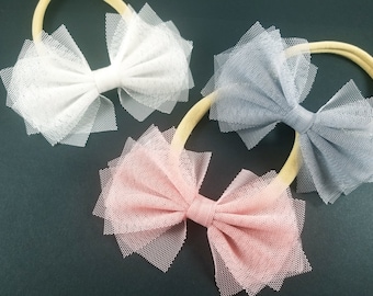 Può includere: Tre fiocchi per capelli in tessuto tulle. I fiocchi sono in bianco, grigio e rosa. I fiocchi sono attaccati a cerchietti elastici.