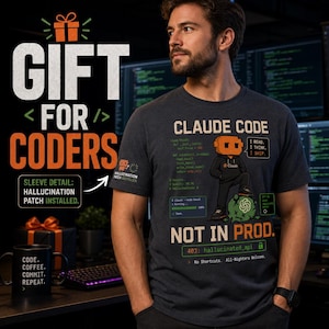 Op de afbeelding: Een donkergrijs t-shirt met korte mouwen en een afbeelding van een pixelachtig personage met een oranje hoofd dat op een groene klodder staat. Het ontwerp bevat de tekst CLAUDE CODE, NOT IN PROD en codefragmenten. Een kleine patch is zichtbaar.