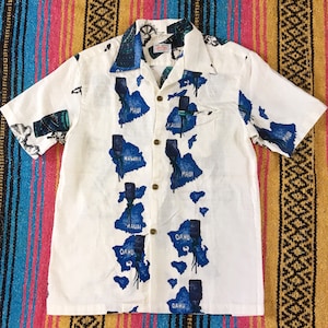 May include: White button-up shirt with a map of the Hawaiian islands printed on it. The islands are labeled with their names: Kauai, Oahu, Maui, and Hawaii.